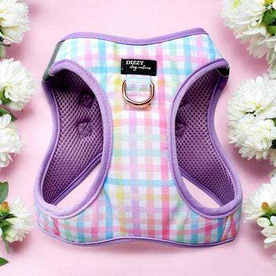 A pastel checkered dog harness with a purple trim and a rose gold D-ring, labelled "Dizzy Dog Collars." The harness is displayed on a pink background surrounded by white flowers.