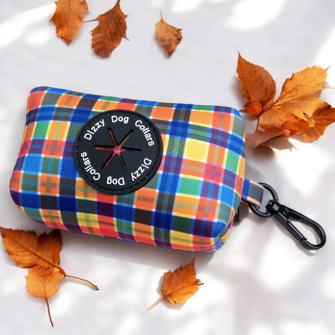 The image features a colorful plaid dog accessory bag on a light surface, accented by autumn leaves. The bag is labeled "Dizzy Dog Collars," and the professional composition highlights the bag, enhanced by the seasonal backdrop of fallen leaves.