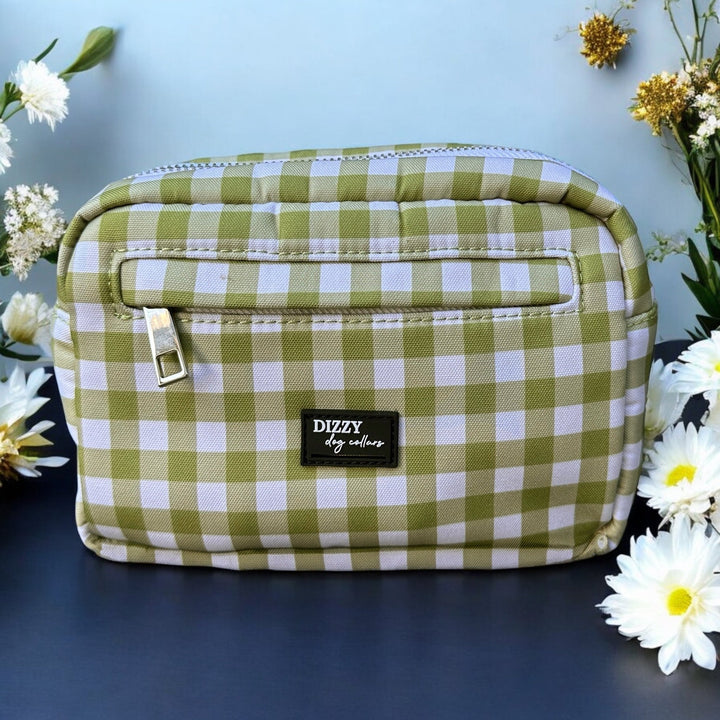 The image features a green and white checkered accessory bag on a light blue background, adorned with white and gold flowers. The bag is labeled "Dizzy Dog Collars," and the composition highlights the bag with an elegant floral touch.