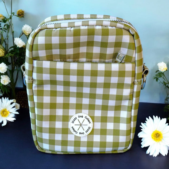 The image features a green and white checkered dog accessory bag on a dark blue surface, accented by white flowers. The bag is labeled "Dizzy Dog Collars," and the professional composition highlights the bag, complemented by the surrounding floral elements.