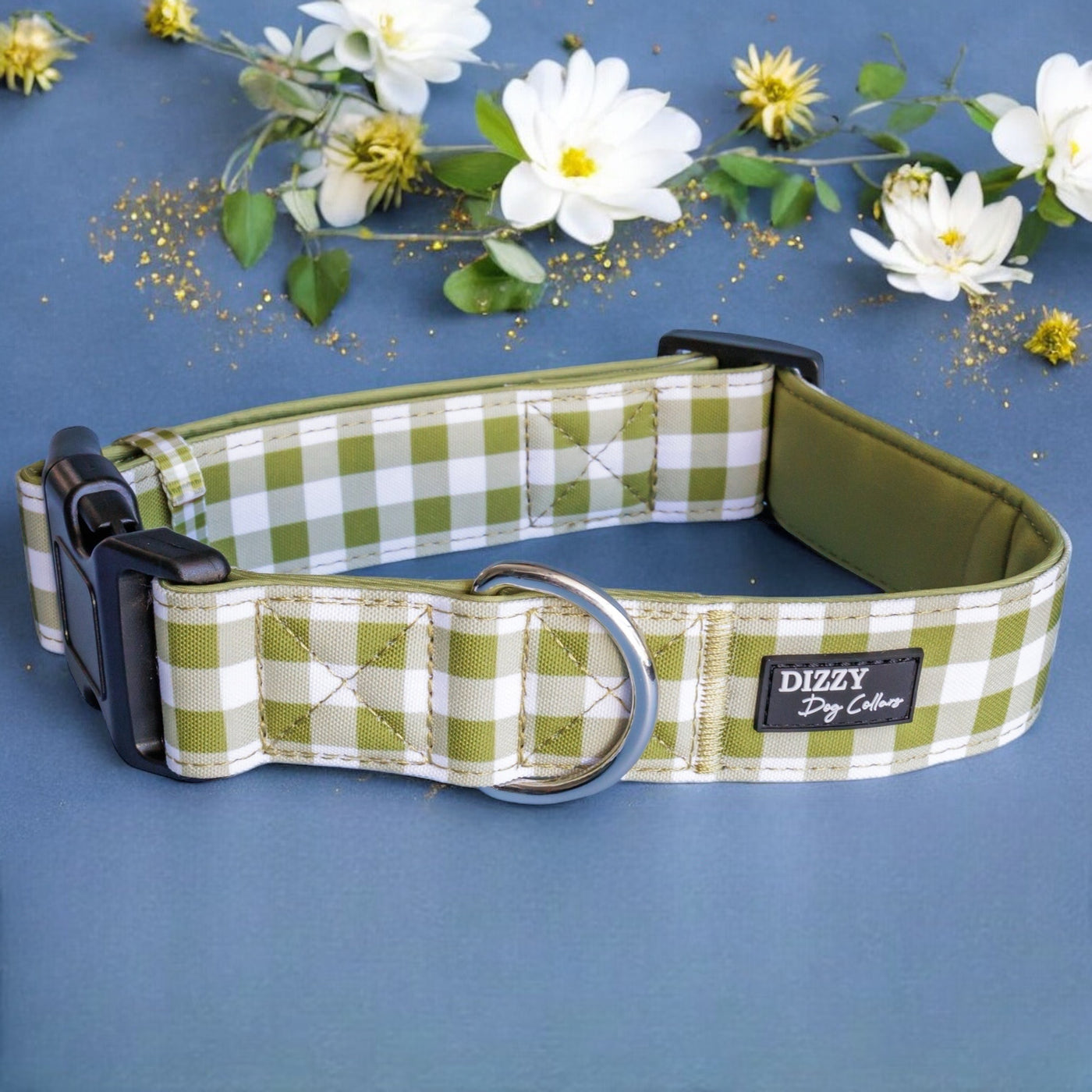 The image displays a green and white checkered dog collar on a navy blue background, adorned with white and gold flowers. The collar features a label that reads "Dizzy Dog Collars." The professional composition of the photo emphasizes the collar, while the floral decorations and gold glitter enhance its visual appeal.