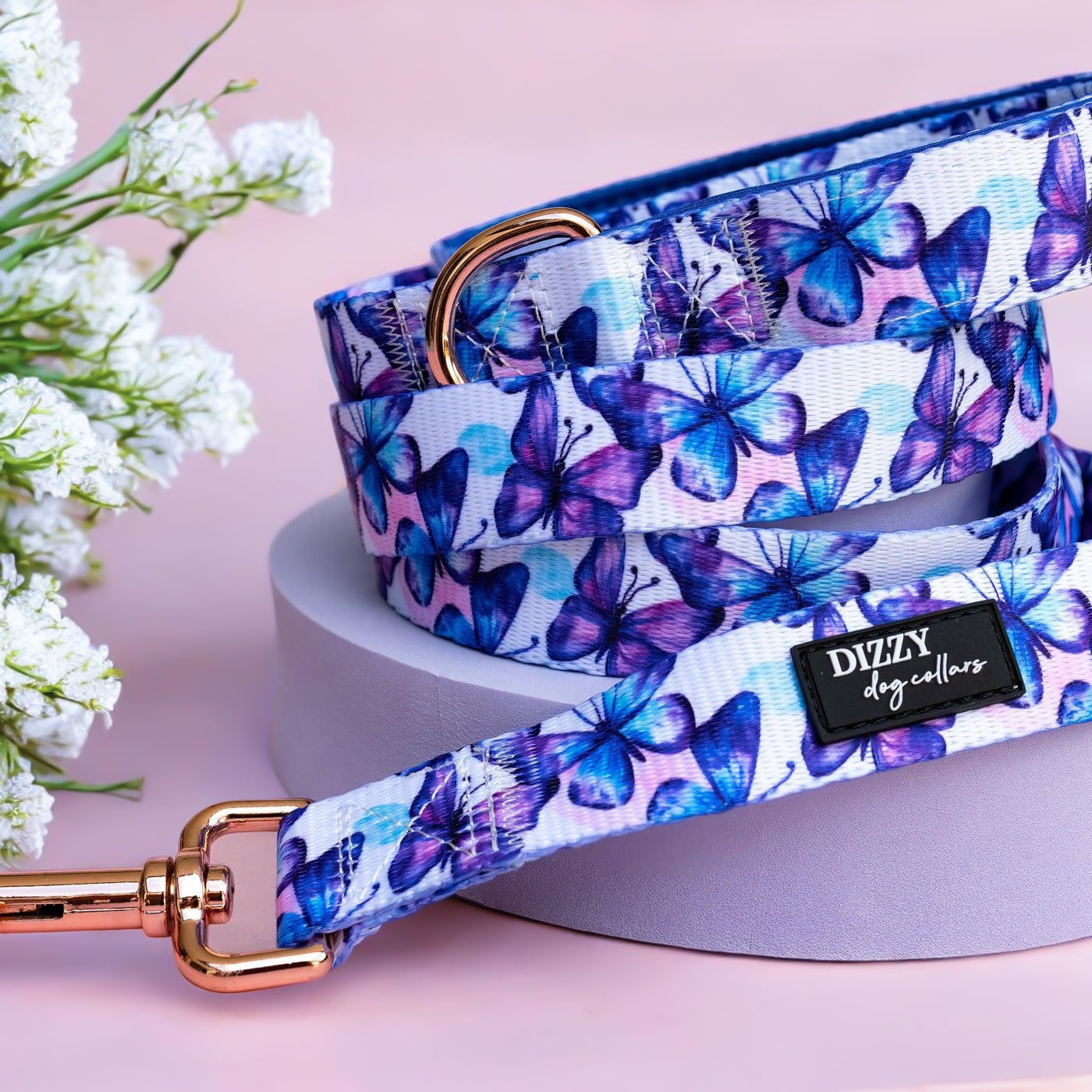 A stylish dog leash adorned with blue and purple butterflies. It includes a sturdy clasp and D-ring, finished in a metallic rose gold tone.